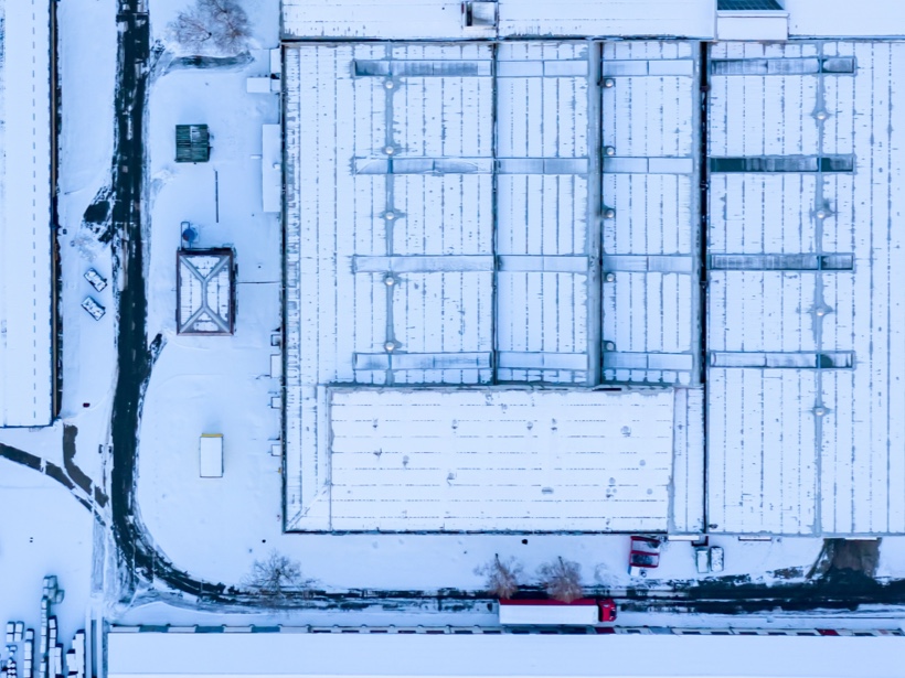 Toiture industrielle enneigée vue du ciel, illustrant l’impact des conditions climatiques hivernales sur la durée de vie d’une toiture commerciale et industrielle.