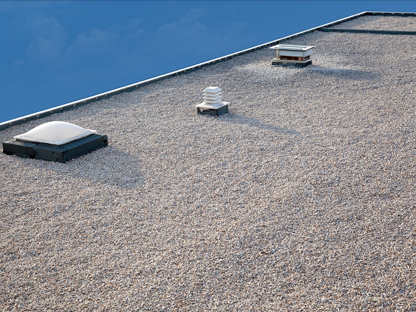 Toiture plate recouverte de gravier avec lanterneaux et évents, illustrant un bon matériau pour votre toiture commerciale offrant durabilité et isolation thermique.