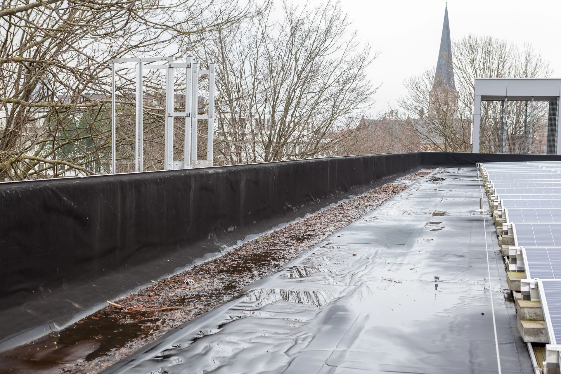 Accumulation d’eau et de débris le long d’un parapet sur un toit plat, près de panneaux solaires installés sur la toiture